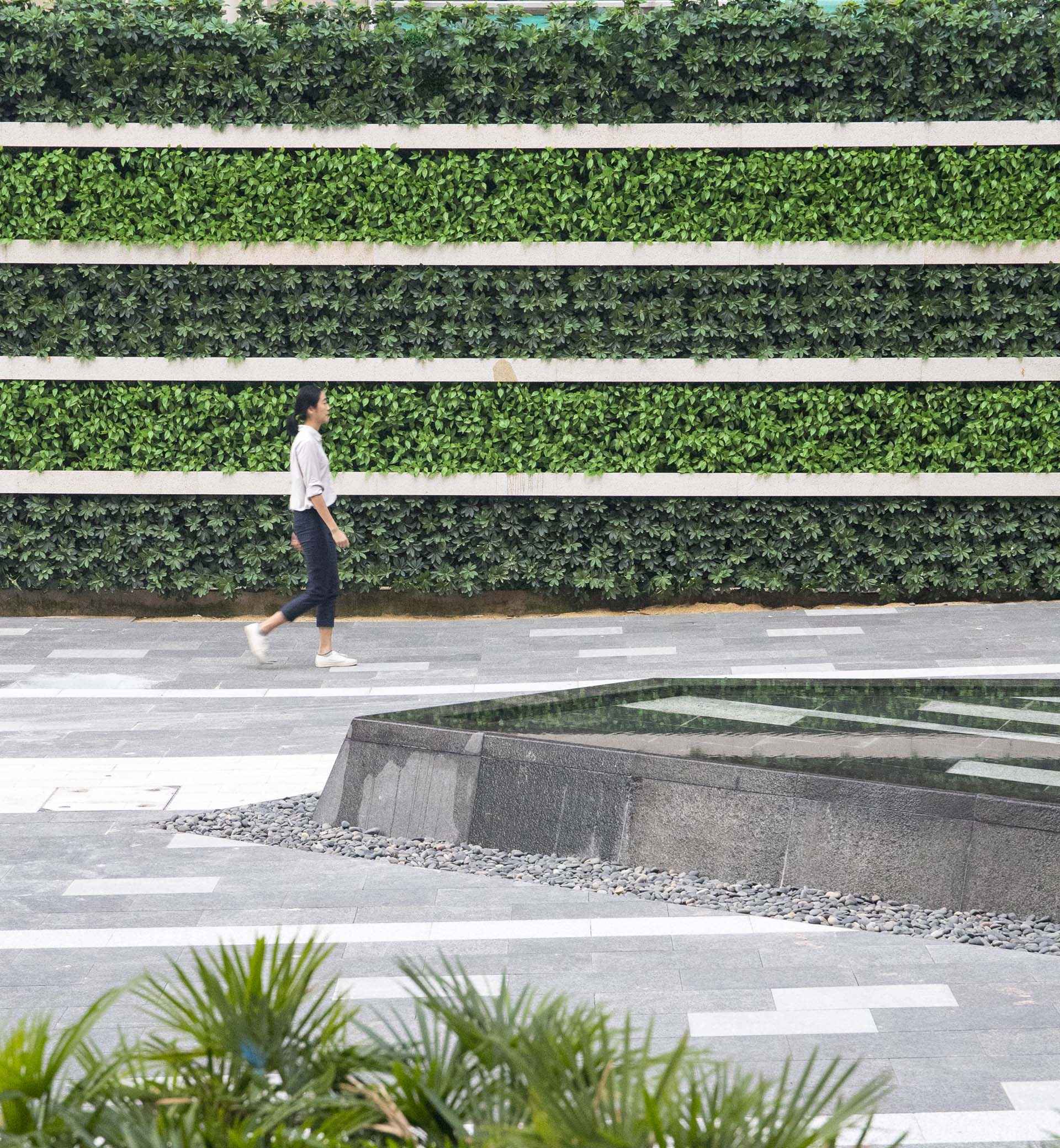 a woman walking past a vertical garden in a city square